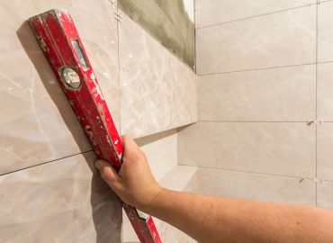 Close-up of worker tiler hand with lever installing on walls ceramic tiles. Tiles installation, tools and home improvement, renovation and construction, comfortable modern home concept.