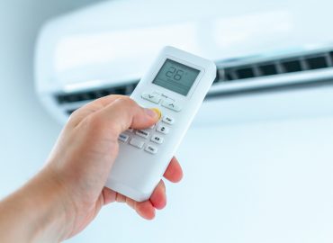 Air conditioner temperature adjustment with remote controller in room at home.